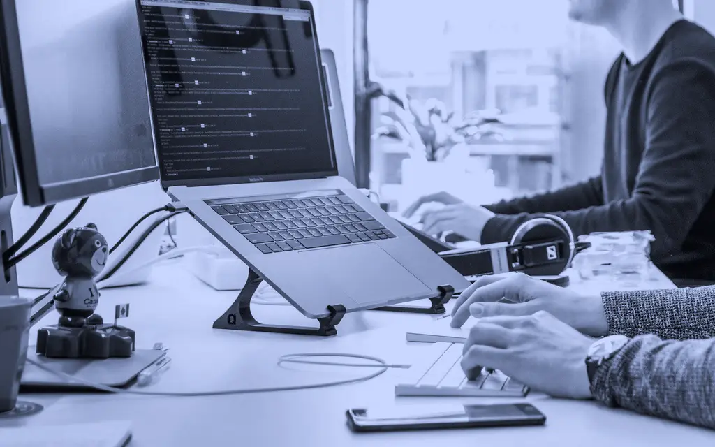 Hands typing on a laptop at a desk in a bright office